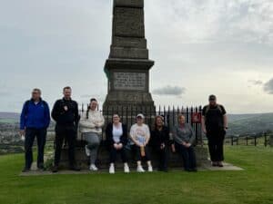 Group of hikers standing in front of a monument after a 10-mile Tameside Peaks hike.
