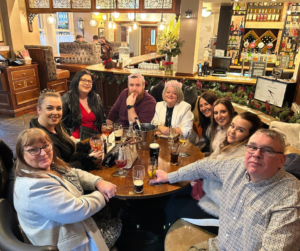 A group of ten people enjoying drinks and conversation at a cozy pub setting.