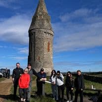 Historic stone tower with group of people in front, outdoor scene.