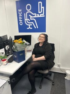 Office worker smiling at desk with flowers and computer.