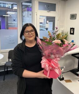 Dedicated staff member holding a large bouquet of flowers in an office setting.