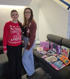 Two women standing beside a table of Christmas gifts and toys.