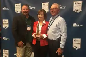 Three people standing in front of a blue banner with an award.