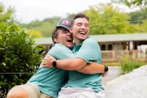 Two men hugging while sitting on a rock.