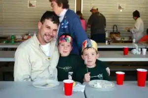 A man and two boys sitting at a table with plates and cups.