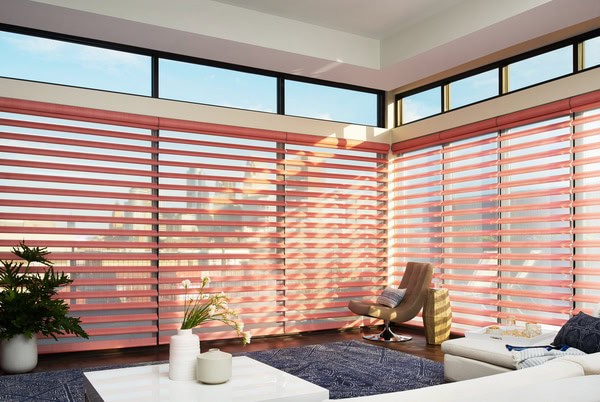 Vivid pink horizontal blinds in a modern sunlit living room with large windows and comfortable seating.