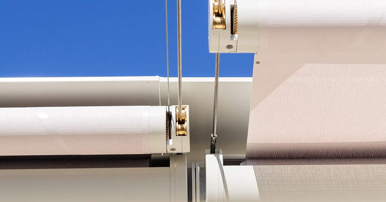 Motorized window blinds on a modern building exterior with a clear blue sky, providing smart shading solutions.