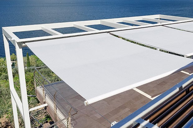 Retractable white fabric awning over balcony with ocean view, UV protection for outdoor shading.