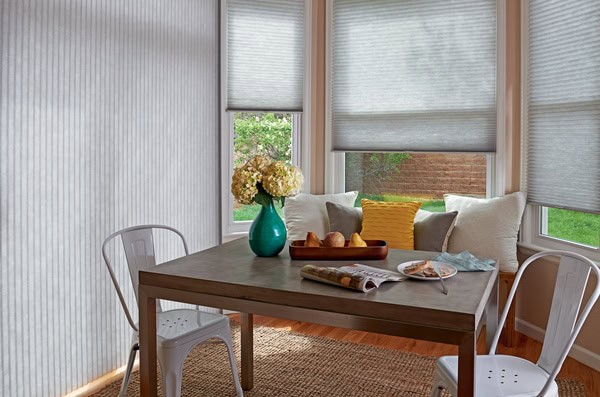 White cellular window shades controlling natural light in a cozy breakfast nook with a wooden table and plush cushions.