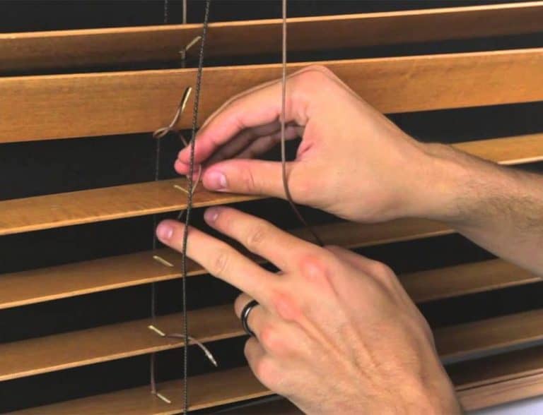Adjusting wooden window blinds with cord, demonstrating blind operation and control.