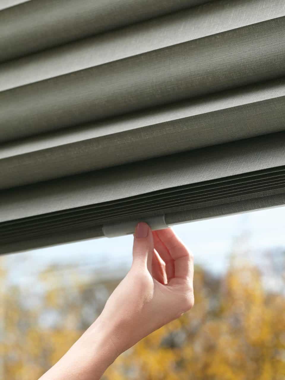 Soft grey window blinds with a close-up of a hand adjusting the mechanism.