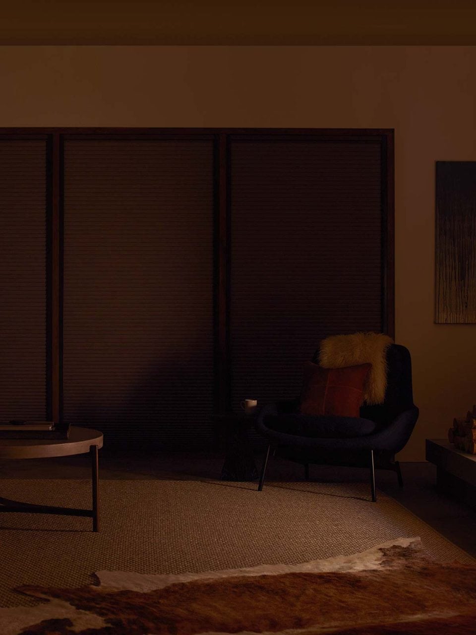 Soft-lit modern living room with a cozy black armchair, fur pillow, and stylish decor.