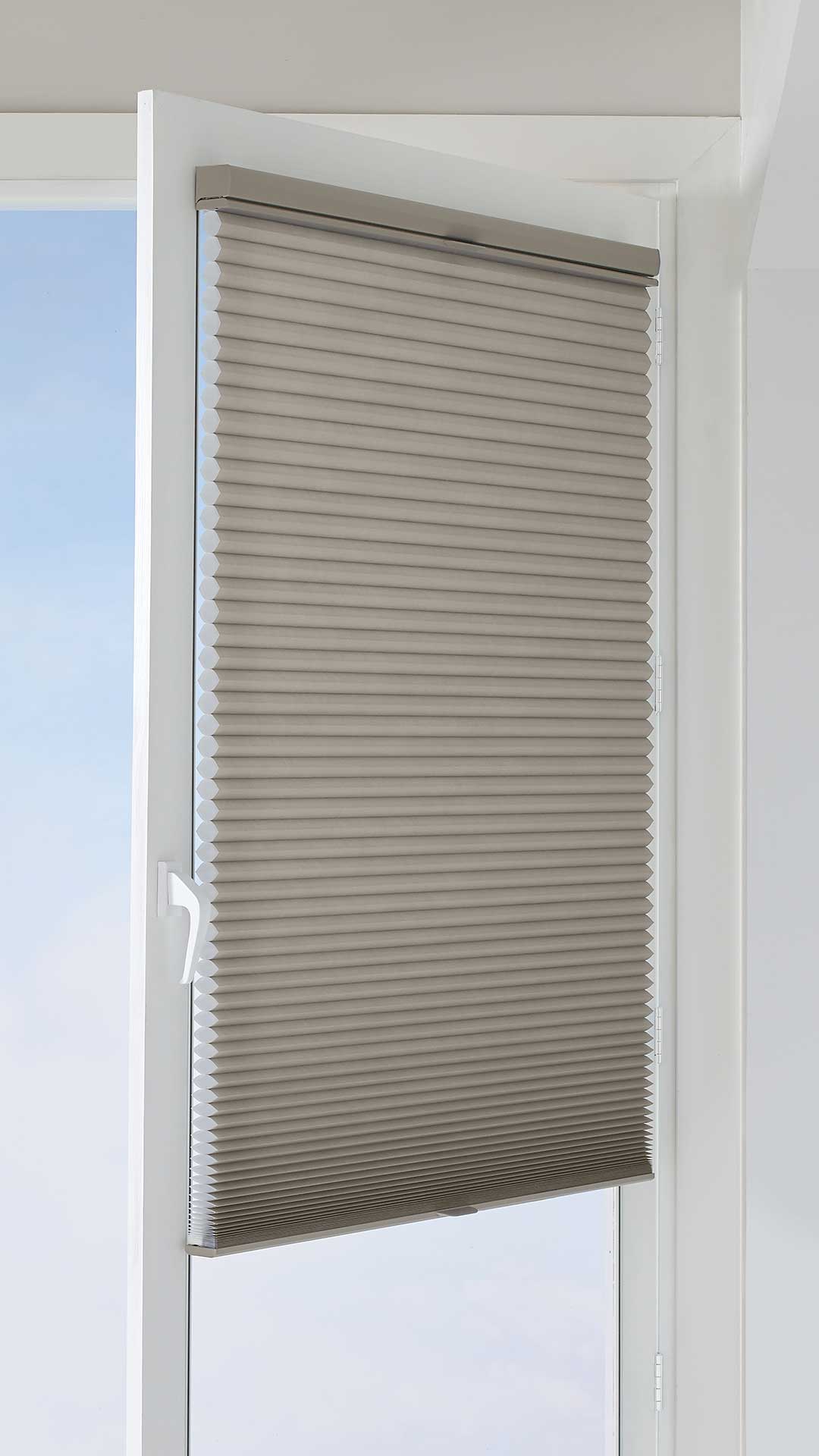 Blue-grey pleated window blind with white frame and handle, providing privacy and light control.