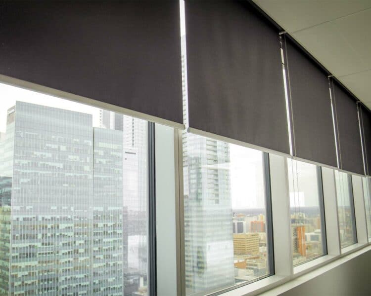 Automatic window blinds in a high-rise office with city skyline view.