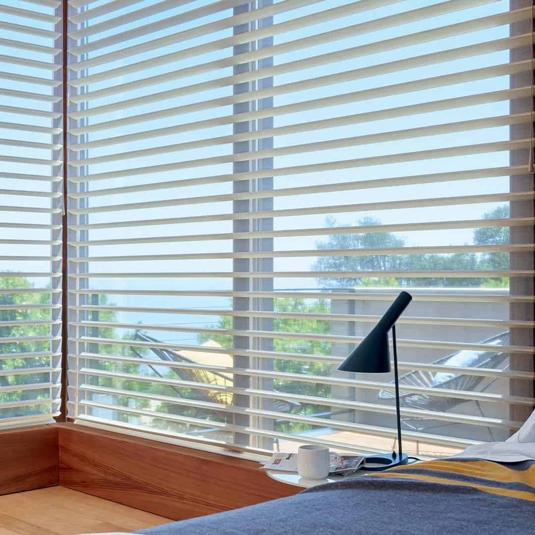 Sunlight streaming through window blinds in a modern bedroom with a view of trees and sky.