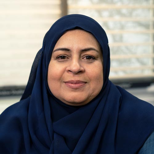 Comfortable woman wearing navy hijab, smiling at camera, modern office background.