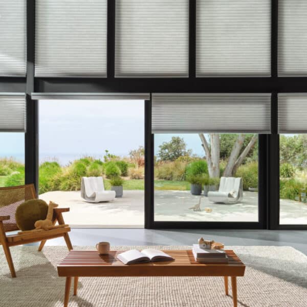 Contemporary living room with large glass sliding doors revealing outdoor garden space with modern chairs and lush greenery.