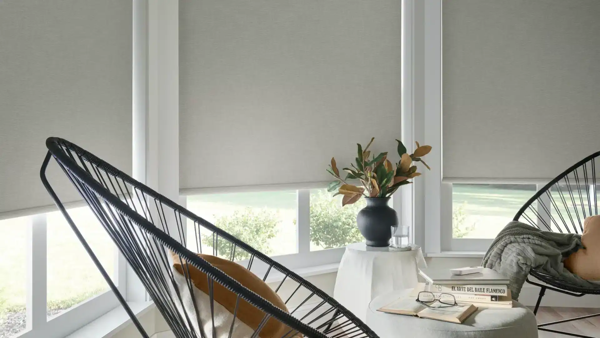 Stylish indoor space with black wire lounge chairs, neutral decor, and large windows with grey blinds.