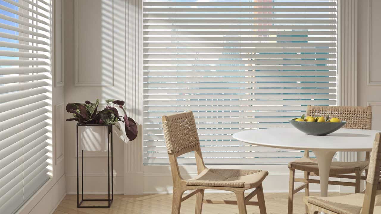 Bright space featuring white window blinds, modern dining table, natural woven chairs, and a decorative plant, creating a cozy, airy atmosphere.