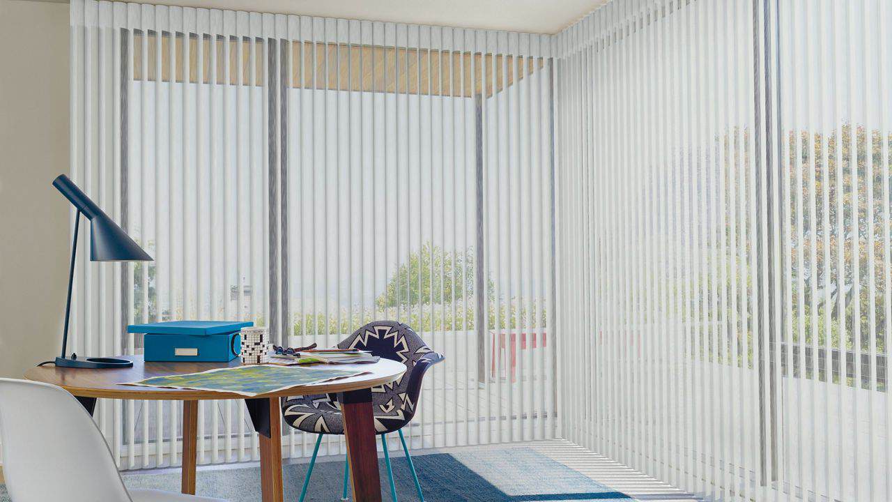 Modern workspace with vertical blinds, desk lamp, and colorful chair offering a relaxing and functional office area, perfect for working or reading.
