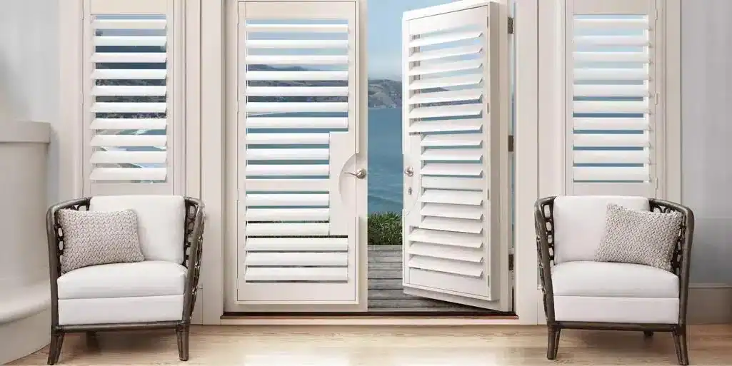 Bright white coastal shutters with scenic ocean view backdrop, opening onto a deck. Elegant indoor seating with cozy pillows complements coastal decor. Perfect for beach house living.
