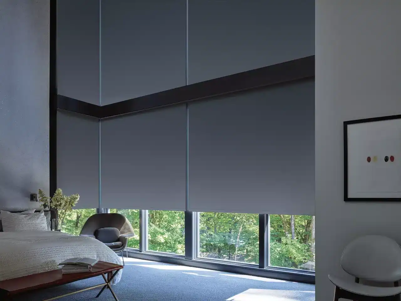 Luxurious bedroom featuring floor-to-ceiling windows with gray roller shades, contemporary furniture, and a serene natural backdrop.