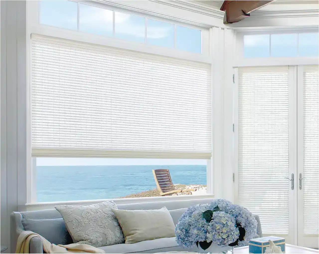 Bright ocean view through white window blinds with beach scenery outside.