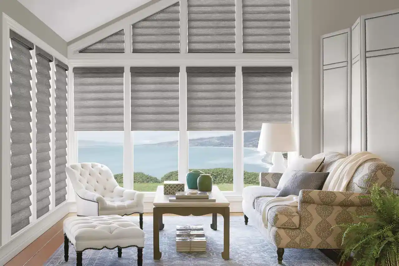 Bright, inviting sunlit room with large windows overlooking the sea, featuring elegant furniture, neutral tones, and stylish window treatments for a relaxing seaside ambiance.