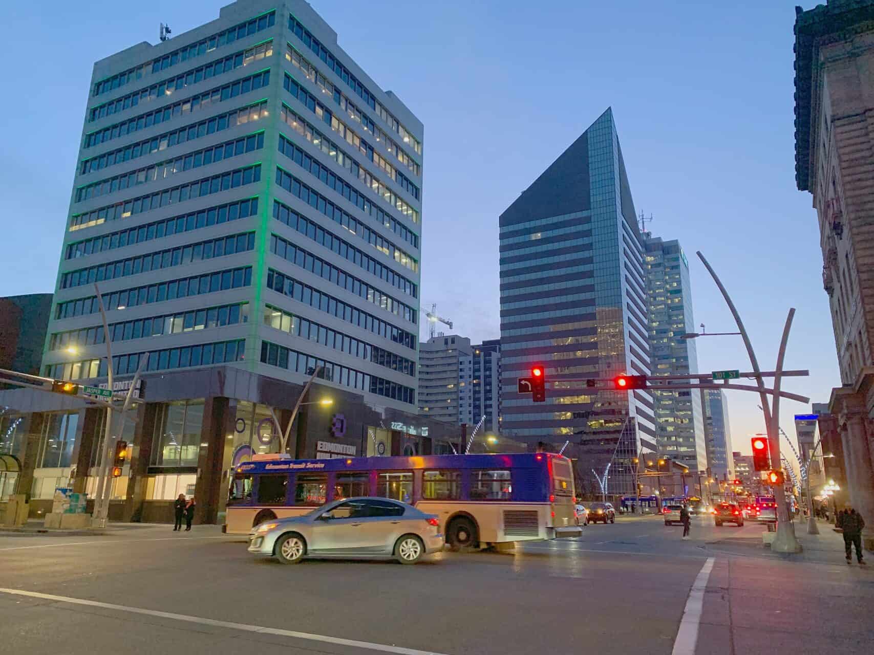 Modern downtown Calgary cityscape with tall office buildings, a bus, and street traffic at dusk in the evening.