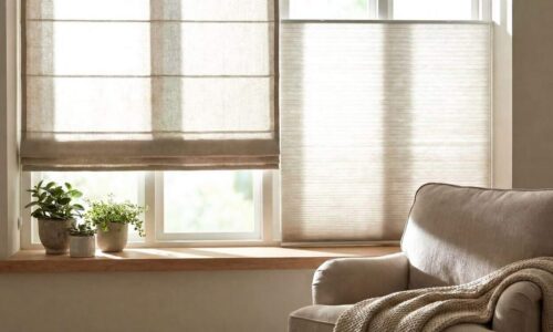 A cozy living room featuring a large window with beige blinds, a comfortable armchair, and potted plants on the windowsill, creating a warm and inviting atmosphere.