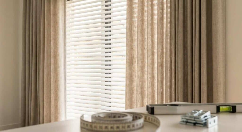 Window with beige curtains and horizontal blinds allowing natural sunlight to brighten the room.