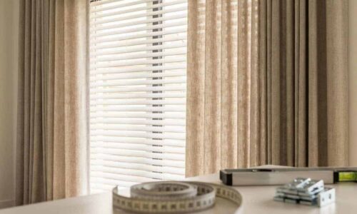 Window with beige curtains and horizontal blinds allowing natural sunlight to brighten the room.