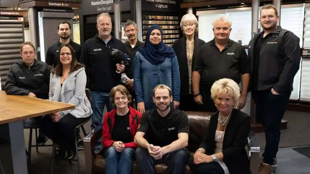 A diverse group of professionals posing together in a retail or service environment, showcasing teamwork and company culture.