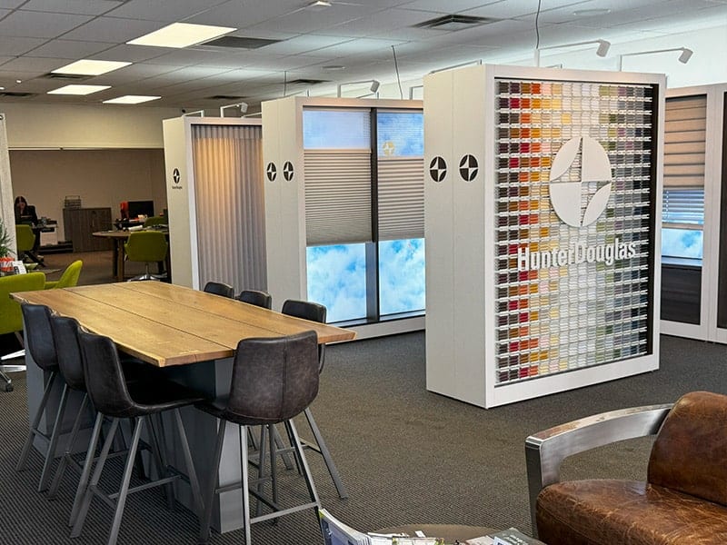 Bright office space featuring window blinds, a large wooden conference table, and Hunter Douglas branding display with color samples for window treatment options.