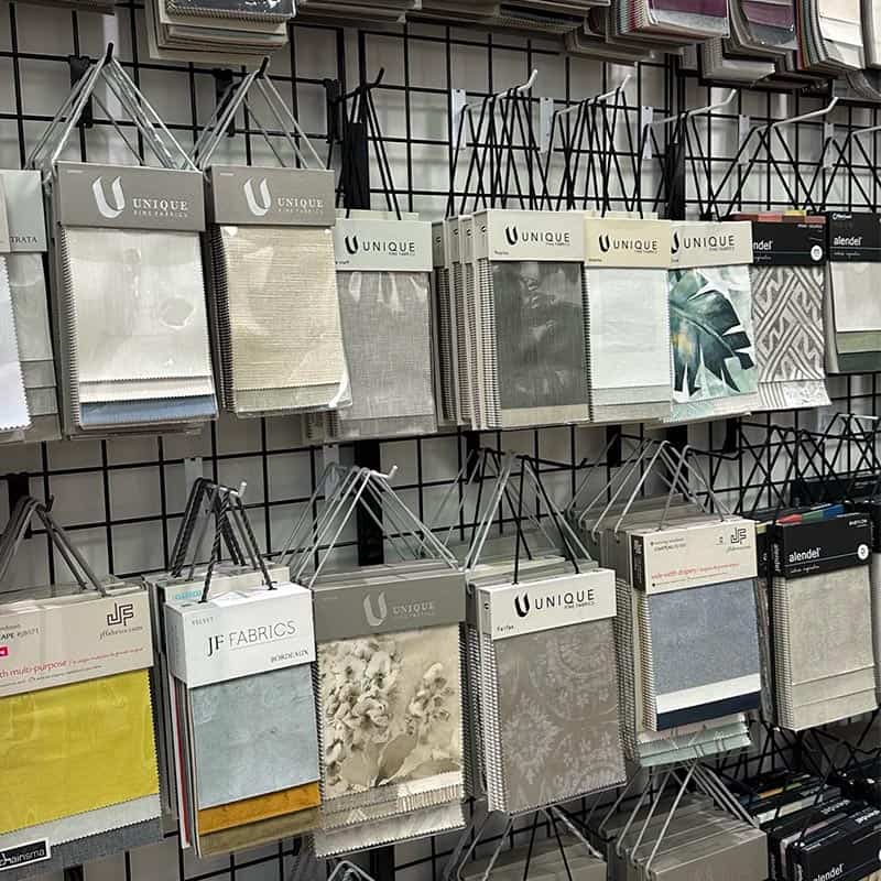 Colorful fabric swatches hanging on a grid wall, showcasing various textures and patterns for interior design or upholstery projects.