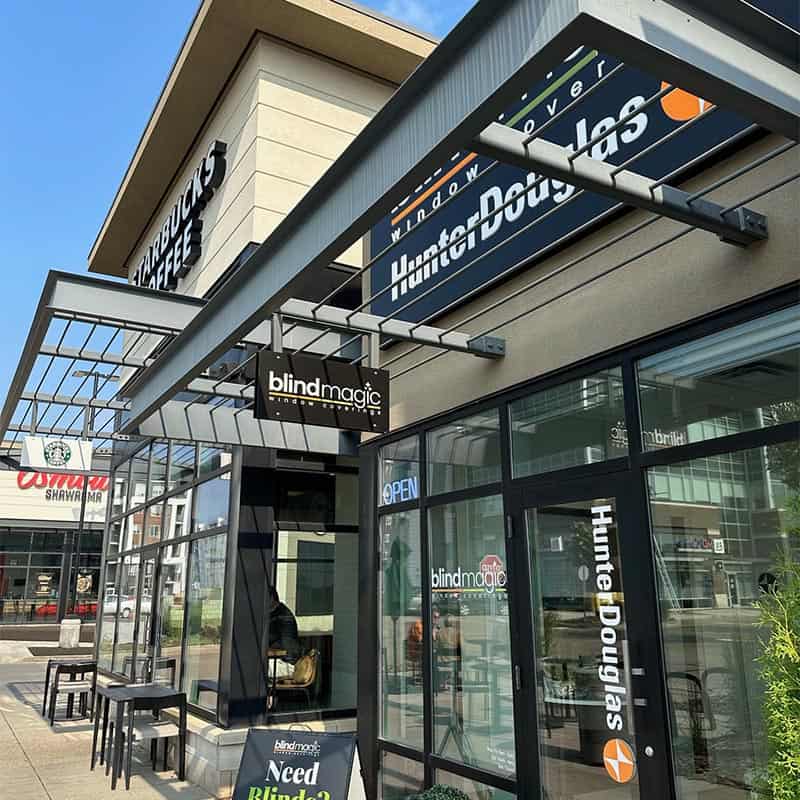 Modern storefront of Blind Magic with outdoor seating and signage, located in a commercial shopping area.