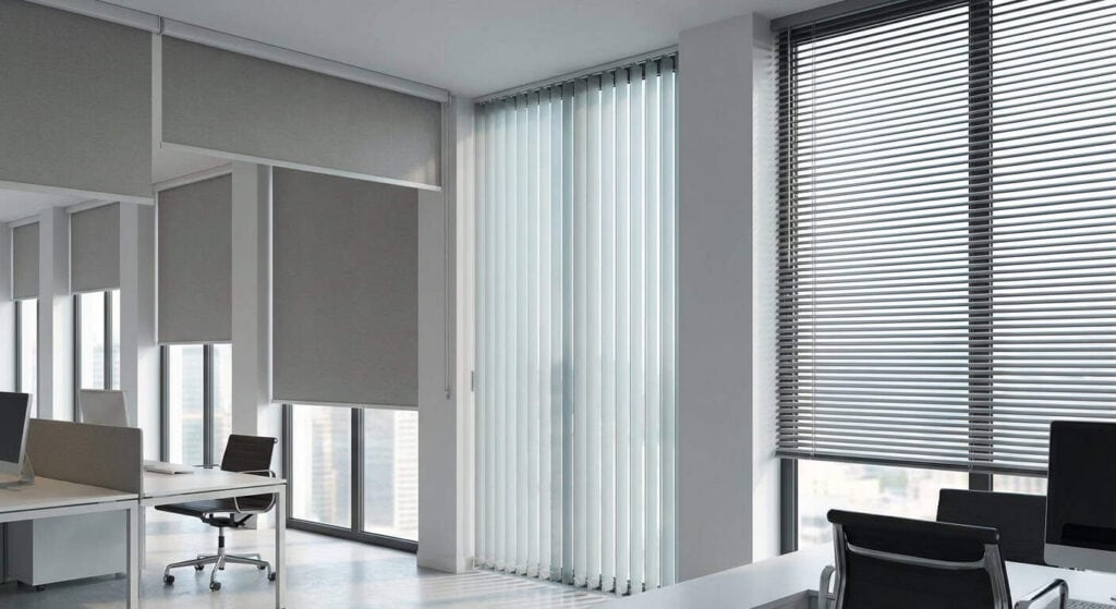Bright office space with large windows and vertical blinds, creating a professional environment with natural light and a view of the cityscape.