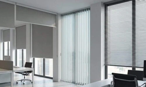 Bright office space with large windows and vertical blinds, creating a professional environment with natural light and a view of the cityscape.