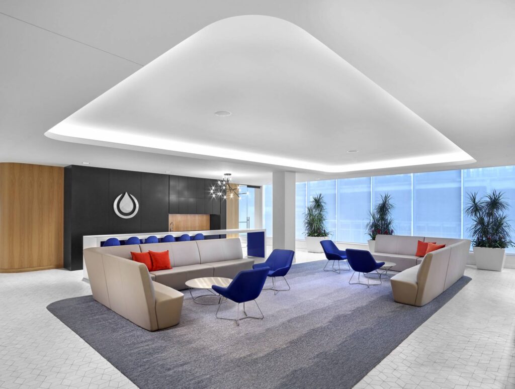 Contemporary office lounge with large windows, stylish seating, and window blinds in a professional environment.