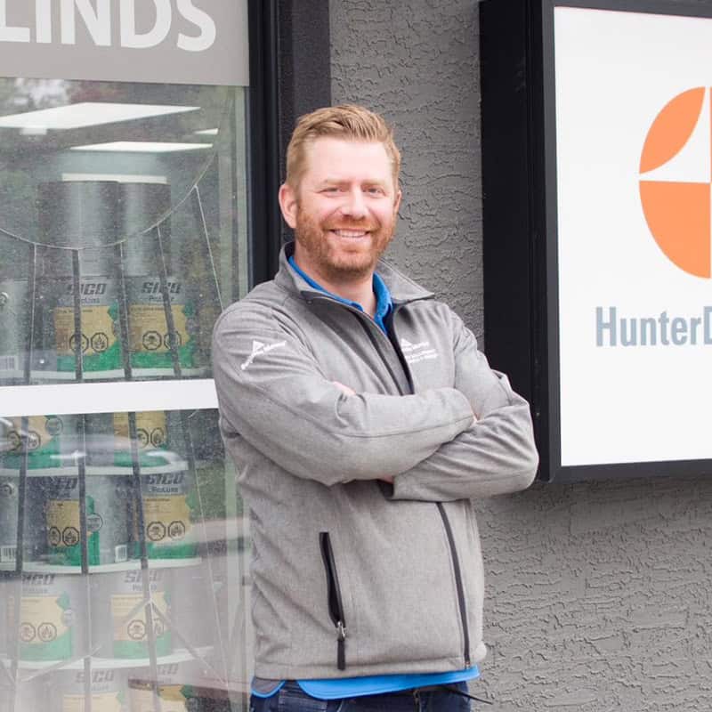 Friendly man standing outside hardware store with crossed arms, wearing a gray jacket.