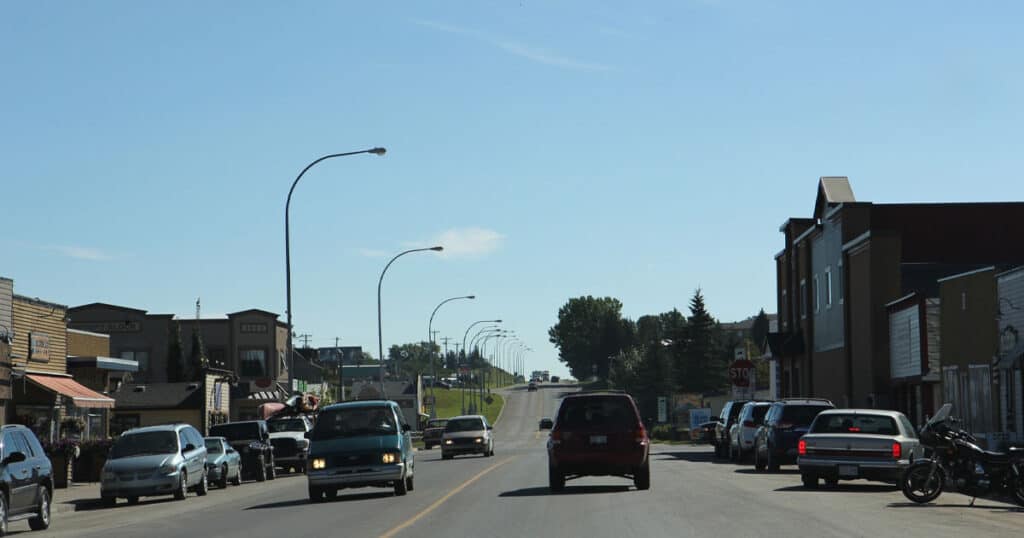 Colorful downtown street with vehicles, storefronts, and street cafes under clear blue sky.