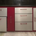 Red kitchen cabinet base with silver drawers and doors, some drawers pulled out, countertop cluttered with appliances on top left and bottles on the right.