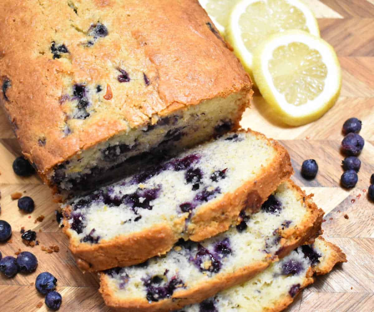 blueberry loaf on a cutting board with blueberries and lemon slices