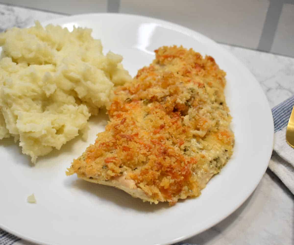 Chicken breast with herbs and cheese on a white plate with mashed potatoes