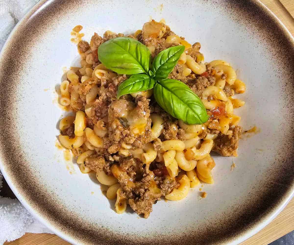 Beef and Macaroni in a stoneware bowl with basil.