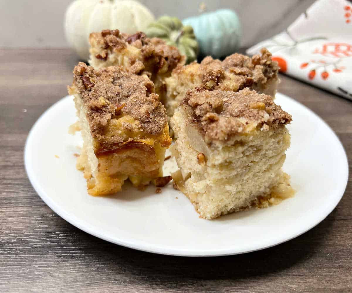 Slices of homemade peach coffee cake with juicy peaches and a crunchy cinnamon pecan topping, served on a white plate.