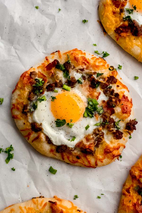 Build Your Own Breakfast Pizzas - Made with pre-made dough for ease and topped with your favorite toppings. We love sausage, bacon, a soft egg, green onion, and extra cheese. It's a brunch party, and you're all invited! #breakfastrecipes #breakfastpizza #pizzarecipes #homemadepizza #brunchrecipes #baconrecipes #bluebowlrecipes | bluebowlrecipes.com A close-up of one of the breakfast pizzas topped with an over easy egg.