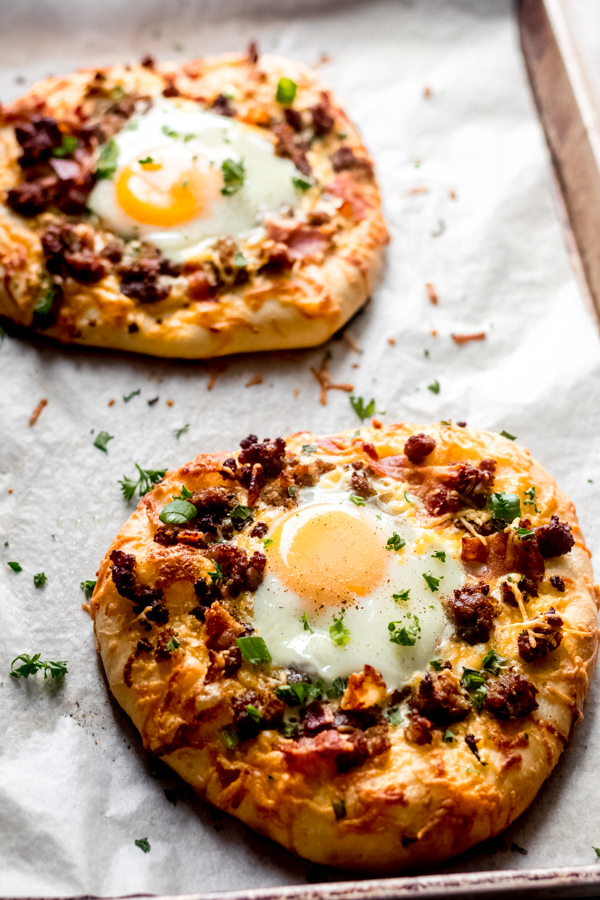 Build Your Own Breakfast Pizzas - Made with pre-made dough for ease and topped with your favorite toppings. We love sausage, bacon, a soft egg, green onion, and extra cheese. It's a brunch party, and you're all invited! #breakfastrecipes #breakfastpizza #pizzarecipes #homemadepizza #brunchrecipes #baconrecipes #bluebowlrecipes | bluebowlrecipes.com Baked breakfast pizzas on a tray.