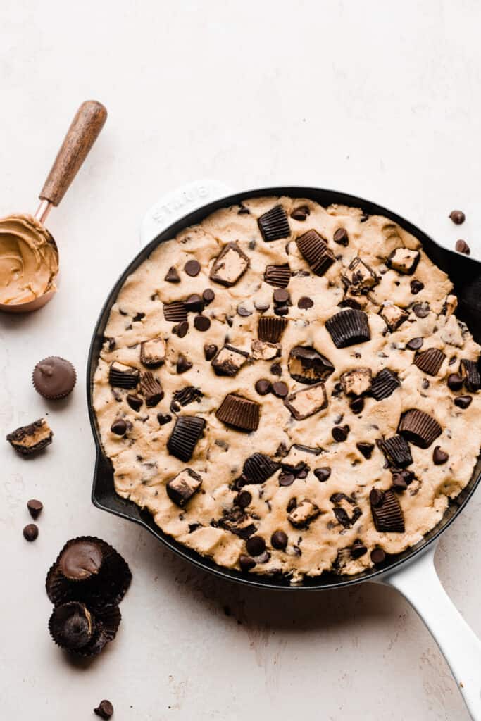 A skillet with the peanut butter cookie dough and studded with chopped peanut butter cups and chocolate chips.