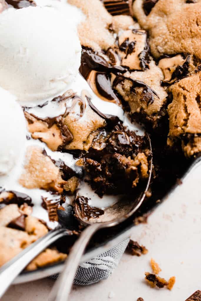 A close-up of a spoon scooping a bite of warm gooey cookie out of the skillet.